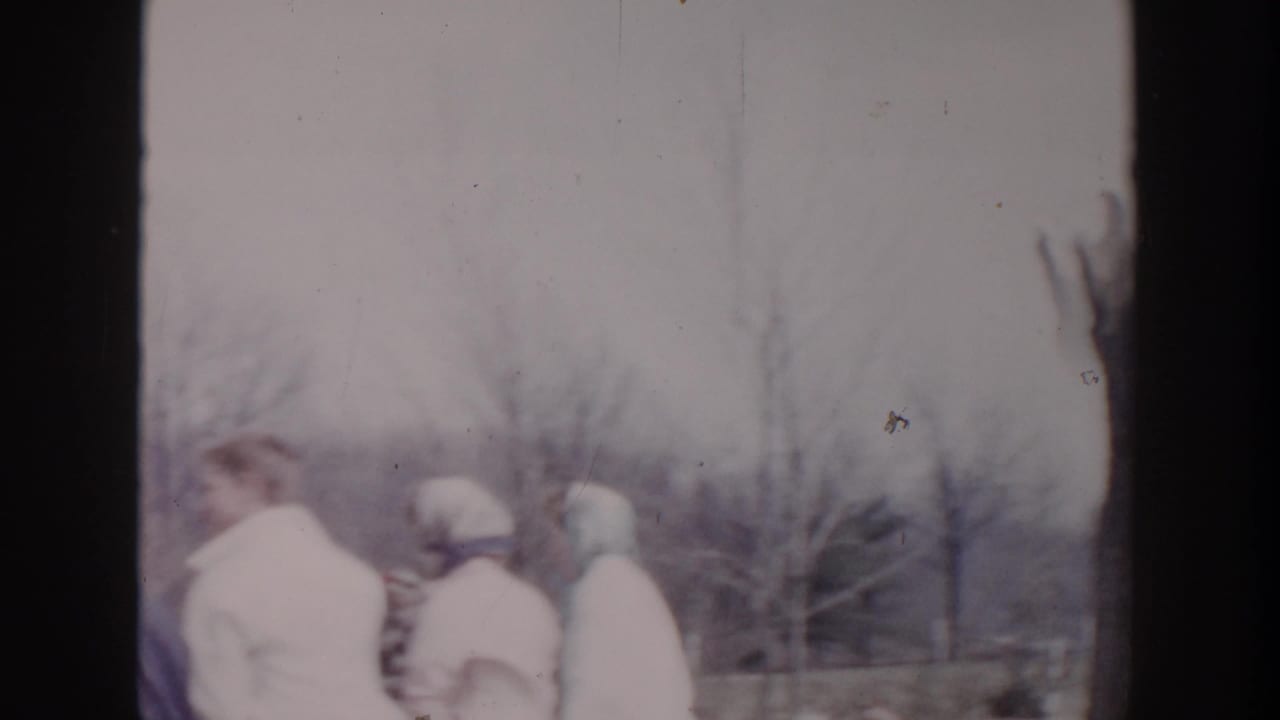 Bundled people walk outdoors near bare trees in a residential area.