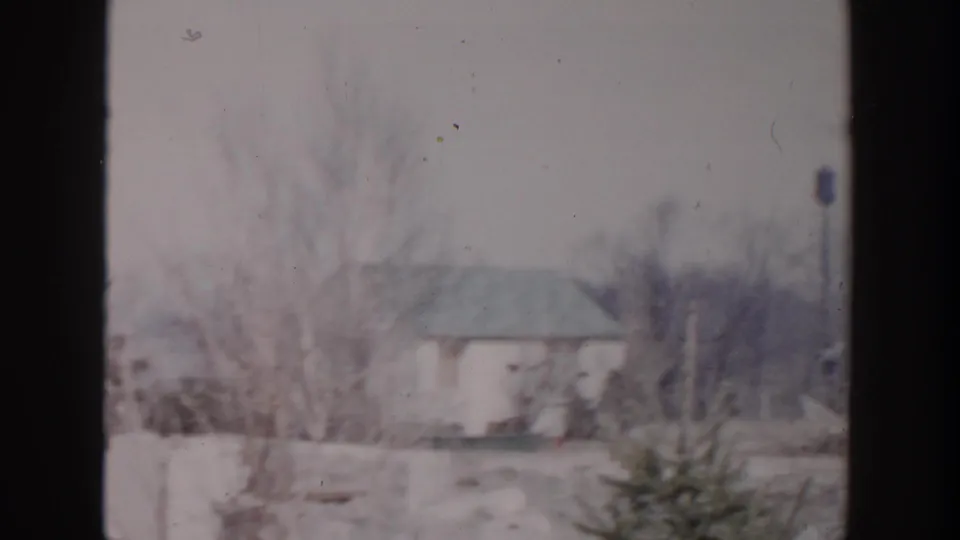 1956 Grand Rapids frame showing a small residential building, bare trees, shrubs, and washed winter light in soft 8mm color.