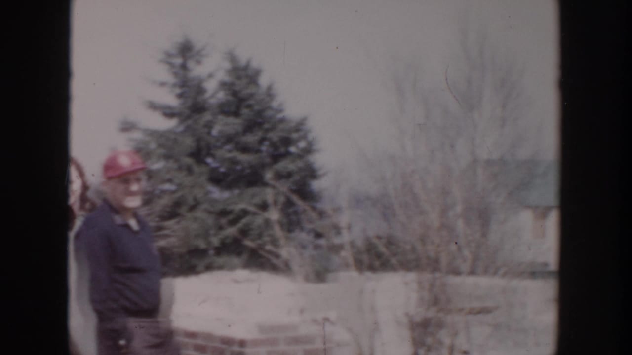 In Grand Rapids-area 1956 home-movie footage, a man in a red cap stands at a snowy outdoor construction site.