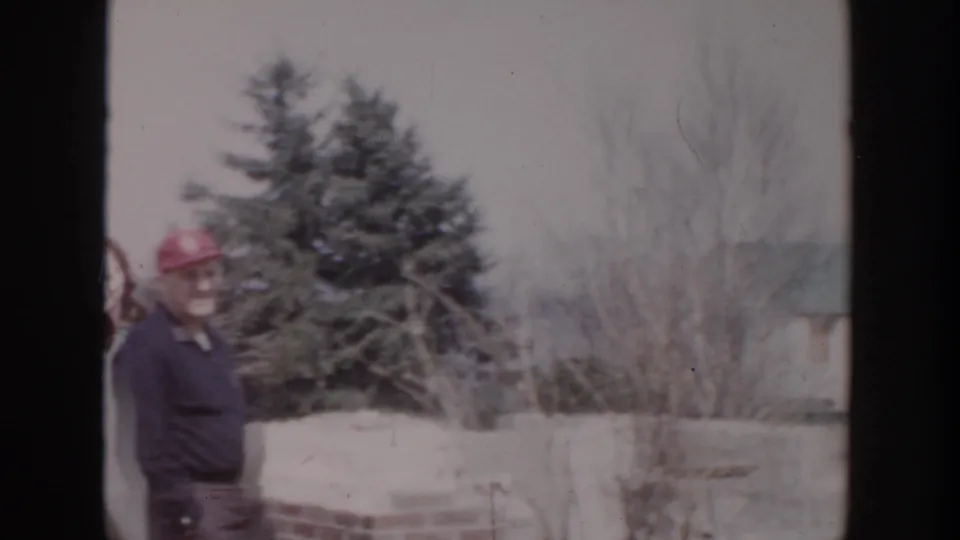In Grand Rapids-area 1956 home-movie footage, a man in a red cap stands at a snowy outdoor construction site.