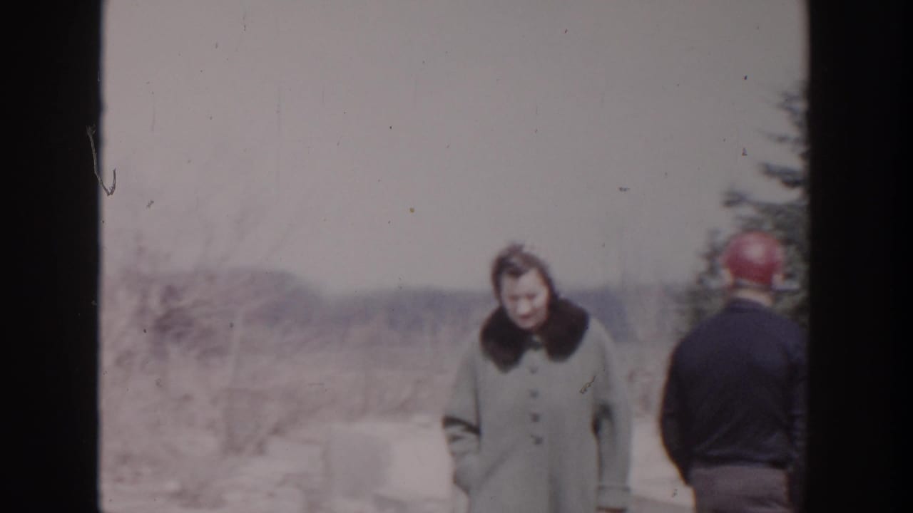 Woman in a light coat stands near a man in a red cap at a snowy site.