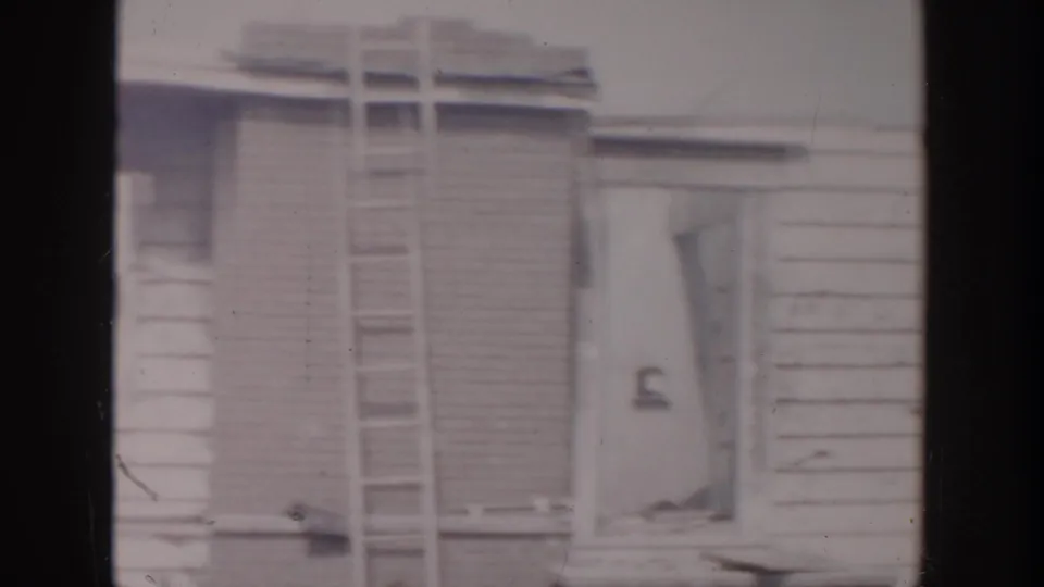 A ladder rests against the wood-sided house, with snowy ground and unfinished exterior details visible.