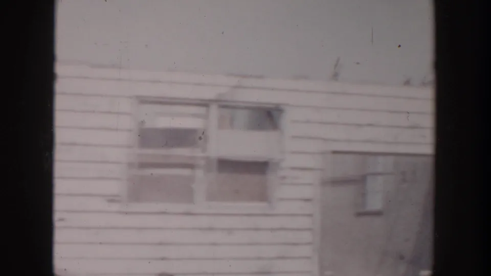 The 1956 home-movie frame shows the house exterior with windows, siding, and a doorway at the construction site.