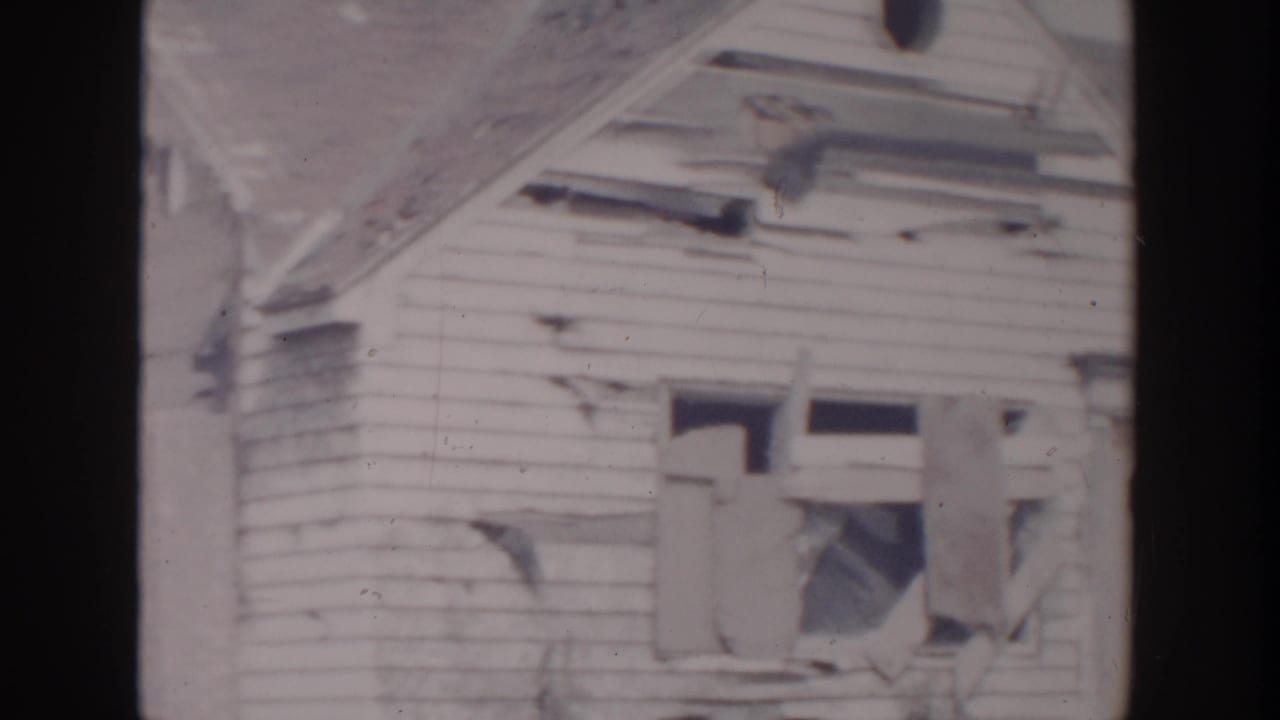 Close view of a damaged house wall with broken windows and torn siding.