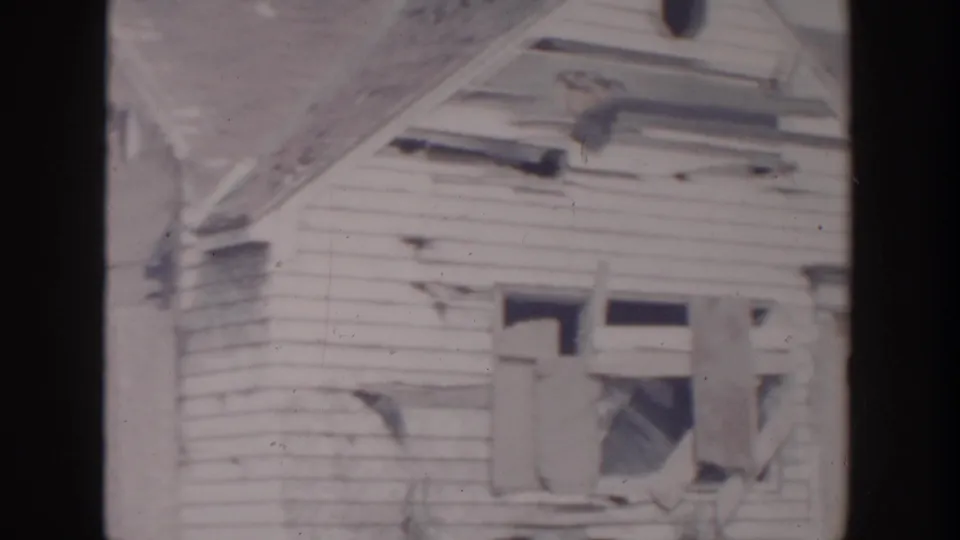 Grand Rapids 1956 frame showing broken windows, damaged clapboard siding, and exposed framing on a residential exterior.