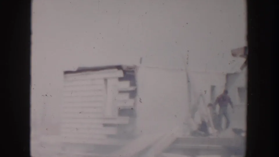 1956 Grand Rapids home-movie frame showing part of the damaged house and a distant man walking near the background.