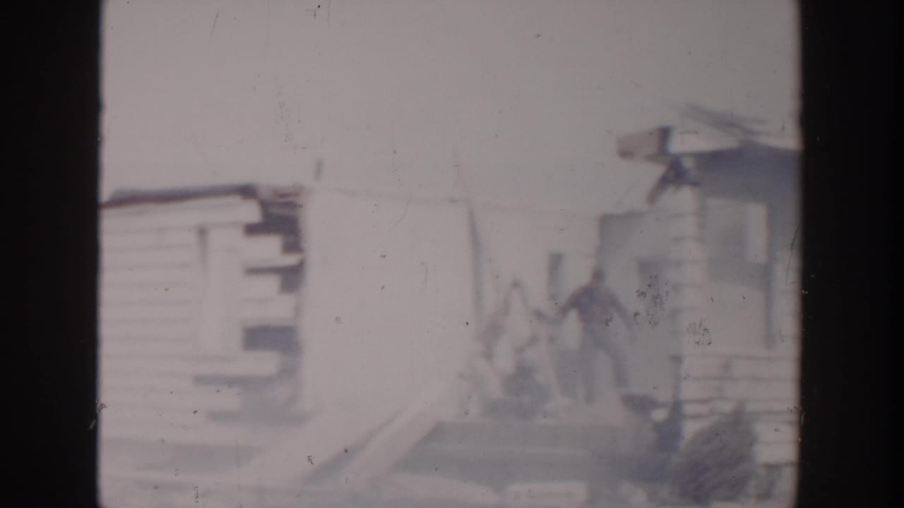 Weathered wooden house with a distant person near damaged siding and blown-out exposure.