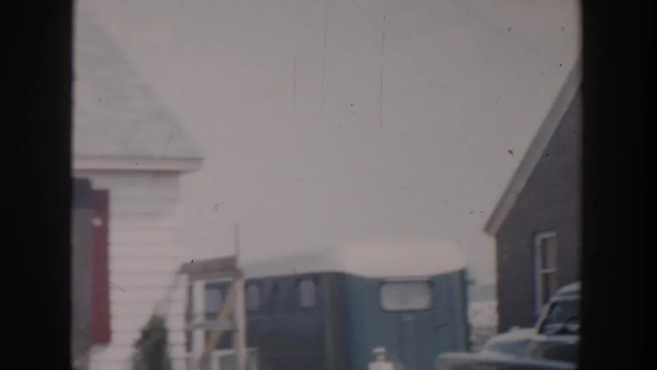 1956 Grand Rapids frame showing a blue trailer-like structure between weathered wooden houses under pale daylight.