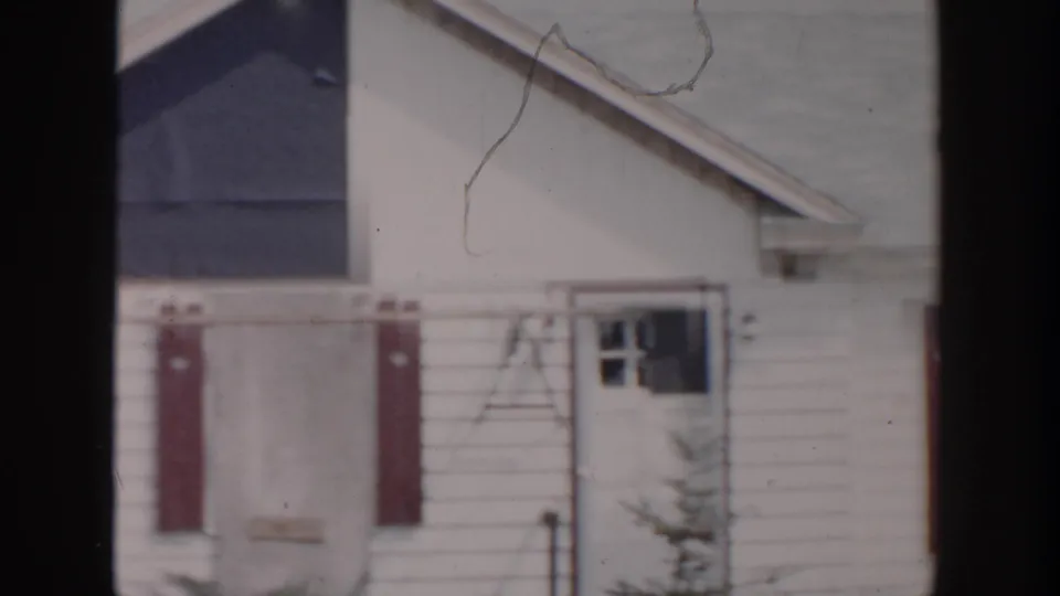 Grand Rapids 1956 frame of a white residential building with red shutters, a damaged door area, and broken window glass.