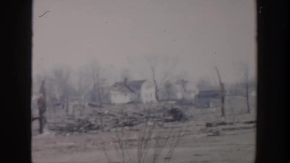 Grand Rapids 1956 aftermath view across an open yard with scattered debris, bare trees, and houses in the distance.