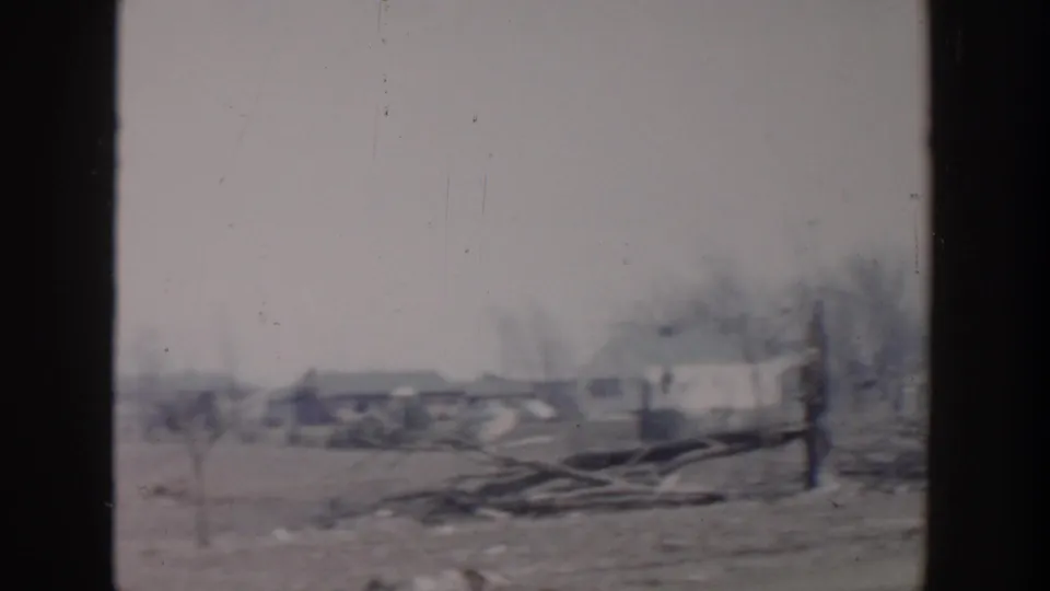 Grand Rapids 1956 home-movie frame showing a wide residential aftermath view with debris piles, bare trees, and low houses.
