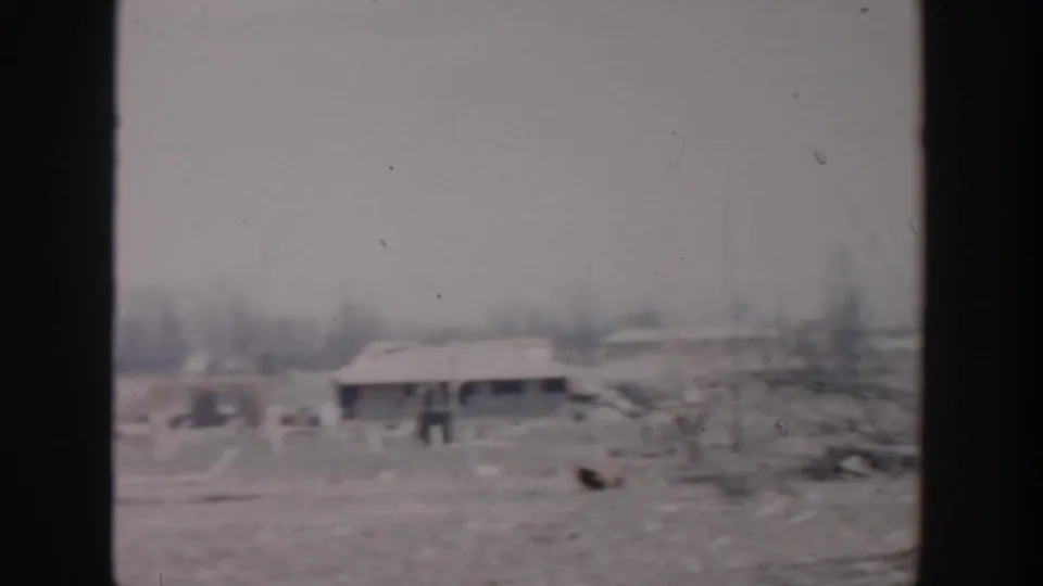 1956 Grand Rapids home-movie view of a low structure near open ground, with scattered debris and bare trees visible nearby.