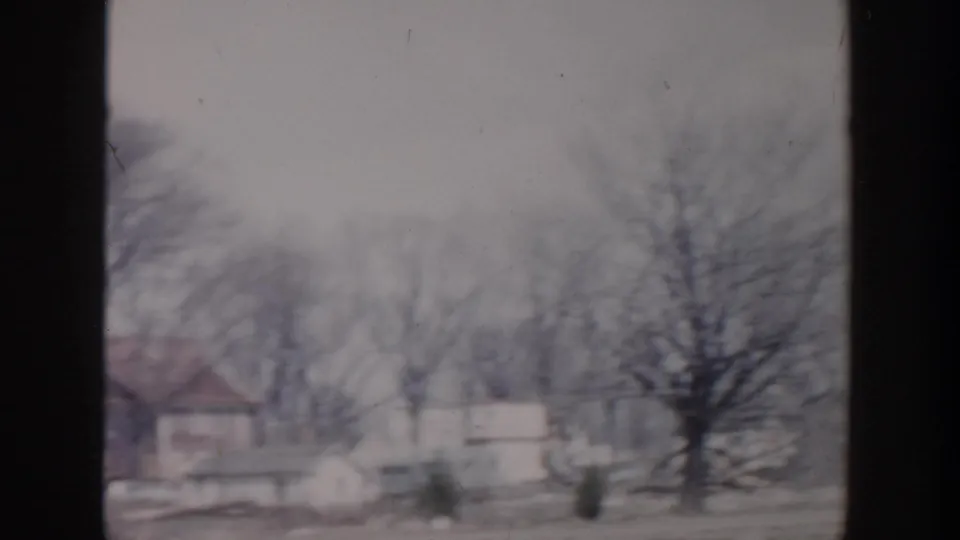 Grand Rapids 1956 home-movie frame showing detached houses and leafless trees along a subdued residential street.