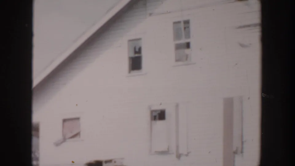 1956 Grand Rapids 8mm frame showing a white house wall with upper window damage, a lower shuttered window, and a side entry.