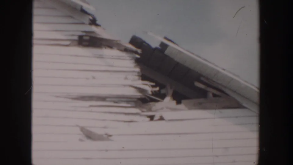 1956 Grand Rapids frame of a white clapboard house exterior with roof damage concentrated near the sloped eaves.