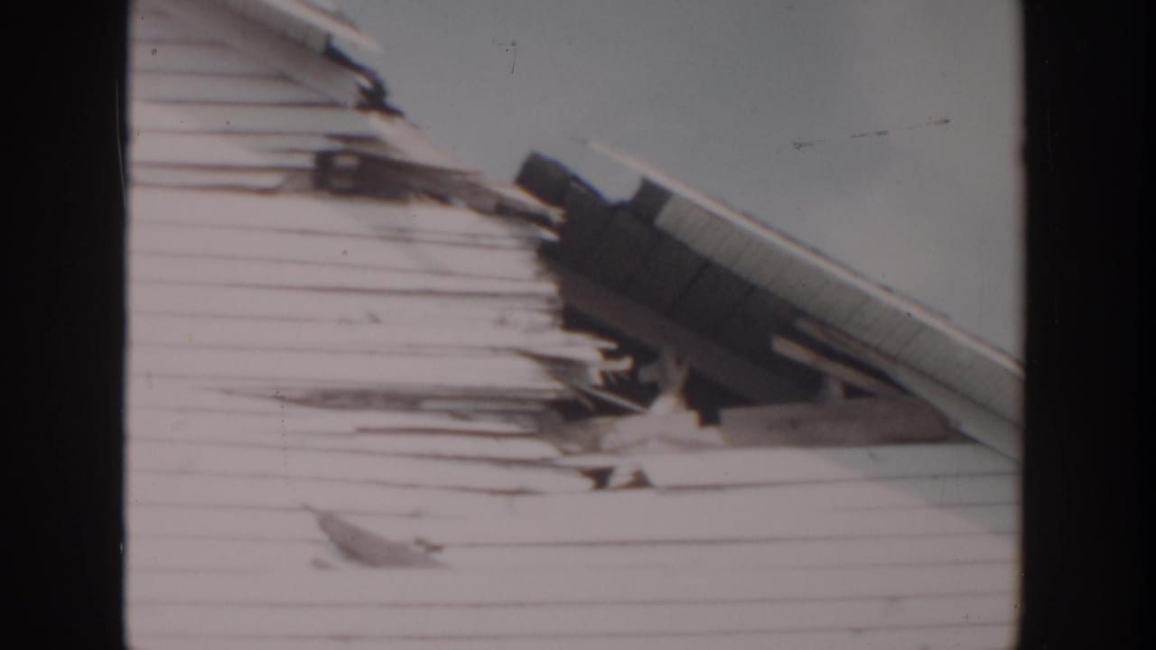 1956 Grand Rapids home-movie frame showing a deteriorated house exterior in winter, with roof damage and snow-softened detail.