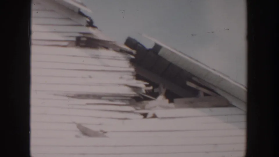 1956 Grand Rapids home-movie frame showing a deteriorated house exterior in winter, with roof damage and snow-softened detail.