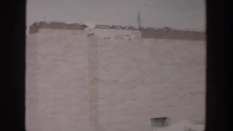 1956 Grand Rapids exterior frame showing a mostly blank brick wall, snow at the base, and a small basement-level opening.