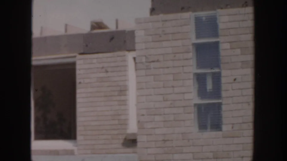 1956 Grand Rapids frame of an unfinished brick facade with an open bay, narrow stacked windows, and dark film gate borders.