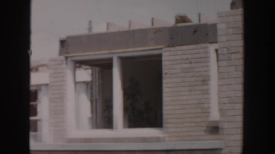 1956 Grand Rapids home-movie view of a brick wall section with window openings, roof edge, and unfinished-looking facade details.