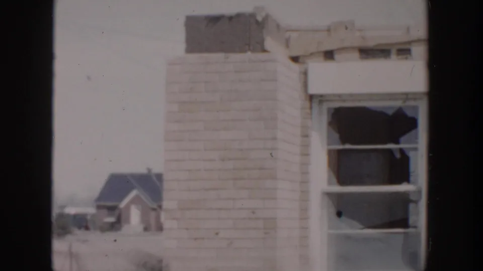 1956 Grand Rapids frame showing a brick house corner, damaged roof edge, broken window, and a smaller house beyond it.