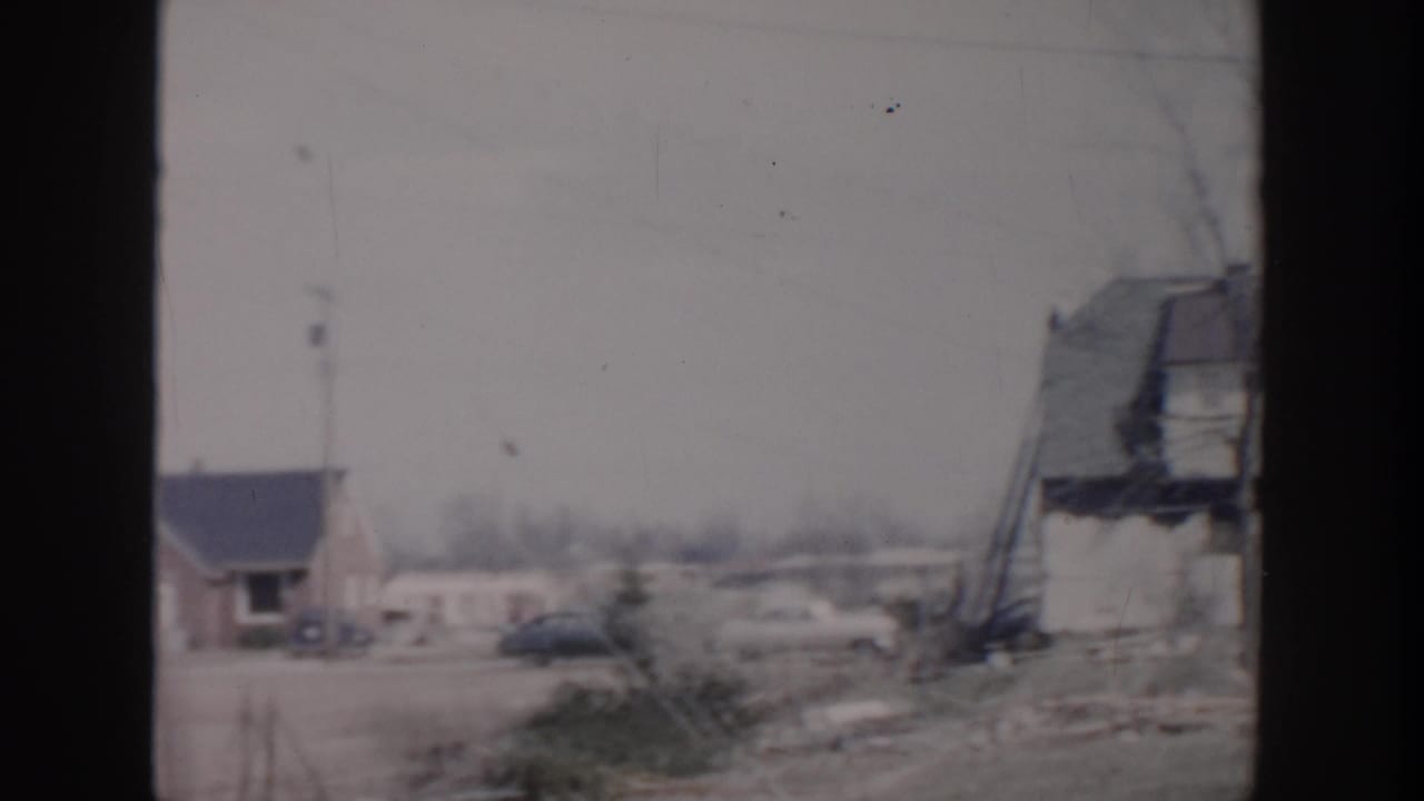 1956 Grand Rapids home-movie frame showing modest houses, bare trees, a parked car, and open roadside ground.
