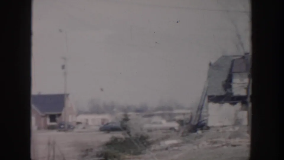 1956 Grand Rapids home-movie frame showing modest houses, bare trees, a parked car, and open roadside ground.