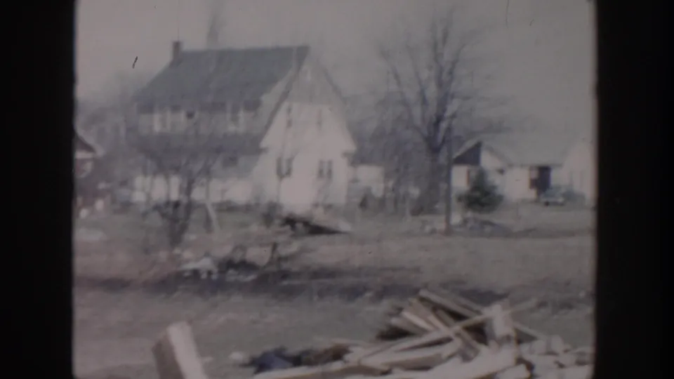1956 Grand Rapids frame showing a light-colored house, open yard, leafless trees, and scattered boards near the foreground.