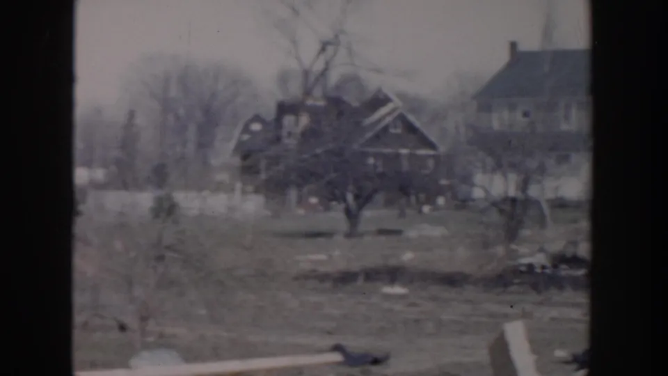 1956 Grand Rapids home-movie frame with a dark house, nearby larger house, bare trees, and open lawn during the pan.
