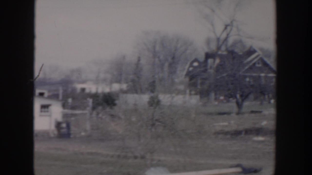 1956 Grand Rapids home-movie view of distant residential buildings, bare trees, a small shed, and scattered debris after storm damage.