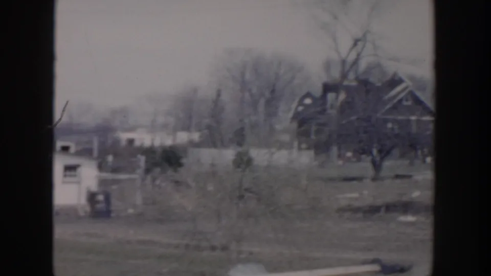 1956 Grand Rapids home-movie view of distant residential buildings, bare trees, a small shed, and scattered debris after storm damage.