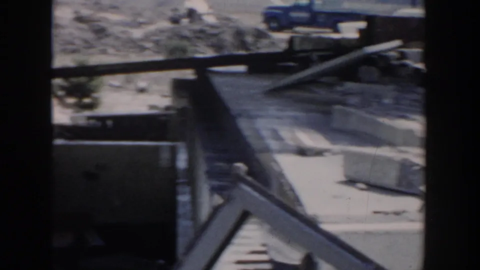 1956 Grand Rapids frame with wreckage, house fragments, a ladder or beam, and a blue truck visible beyond the damaged area.
