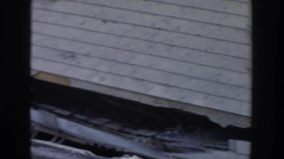 Close 1956 Grand Rapids view of torn roof material and siding on a damaged residential structure.