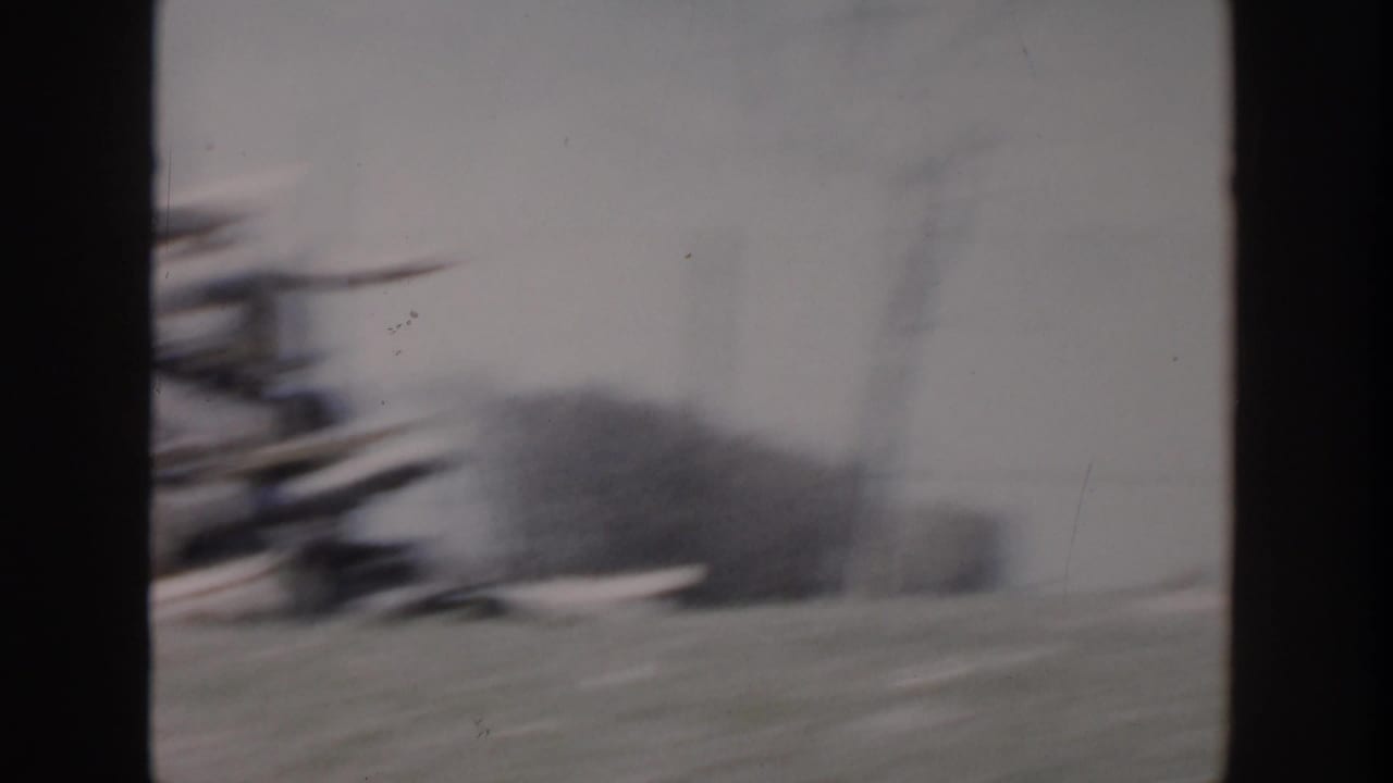 1956 Grand Rapids home-movie frame showing a blurred damaged residential area through dark window-like dividers.