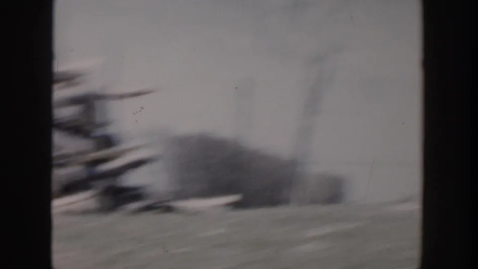 1956 Grand Rapids home-movie frame showing a blurred damaged residential area through dark window-like dividers.