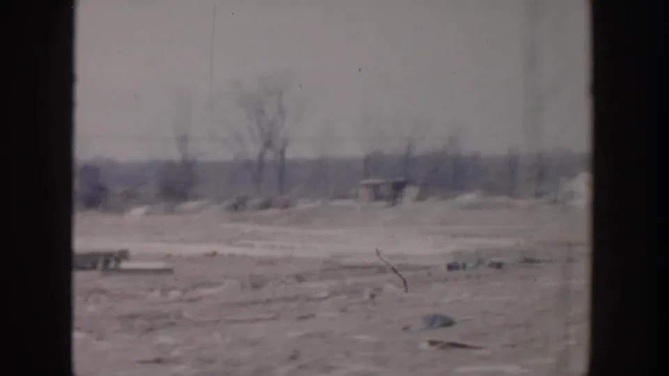 Grand Rapids aftermath view with bare trees, scattered debris, low distant structures, and dark frame borders.