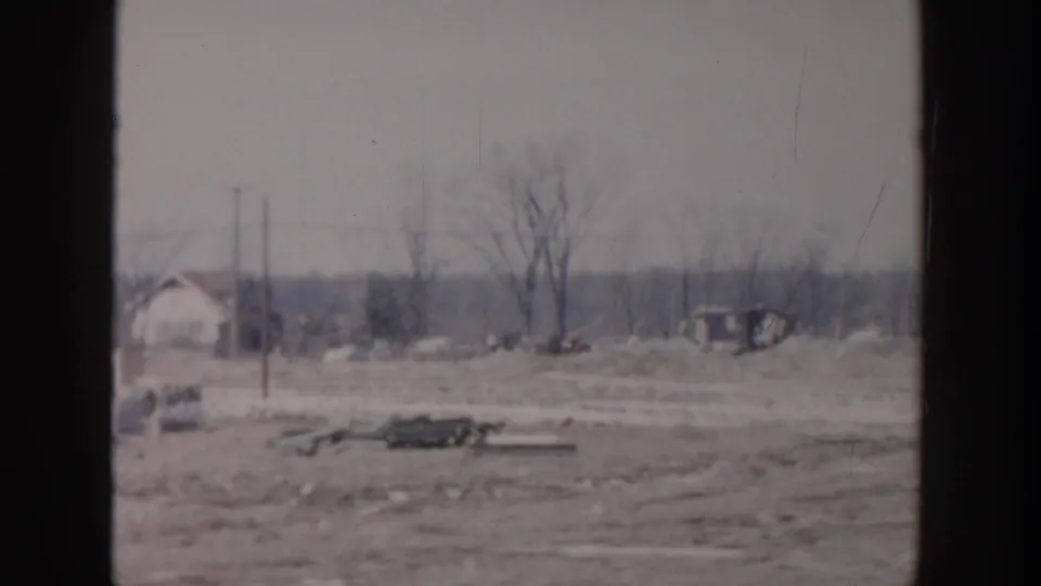 1956 Grand Rapids aftermath frame showing debris, utility poles, bare trees, low structures, and two small figures.
