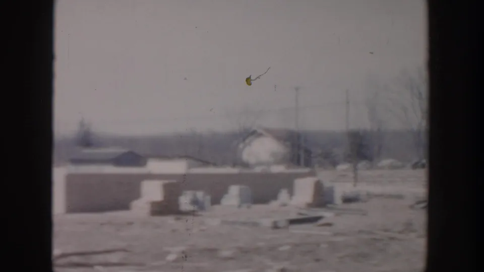 Grand Rapids aftermath view with a low damaged structure, scattered materials, distant houses, and bare trees.