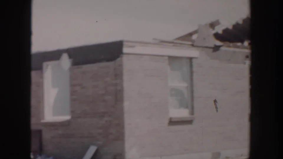 1956 Grand Rapids frame showing the side of a brick residential building with missing roof sections and a visible window.