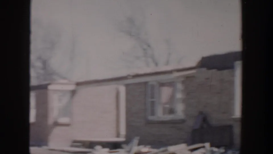 Grand Rapids 1956 home-movie view of a damaged residential wall with windows, loose boards, and yard debris.