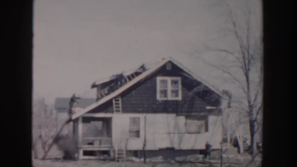 Grand Rapids 1956 home-movie frame showing a weathered two-story house with ladders, workers, bare trees, and a street-facing porch.