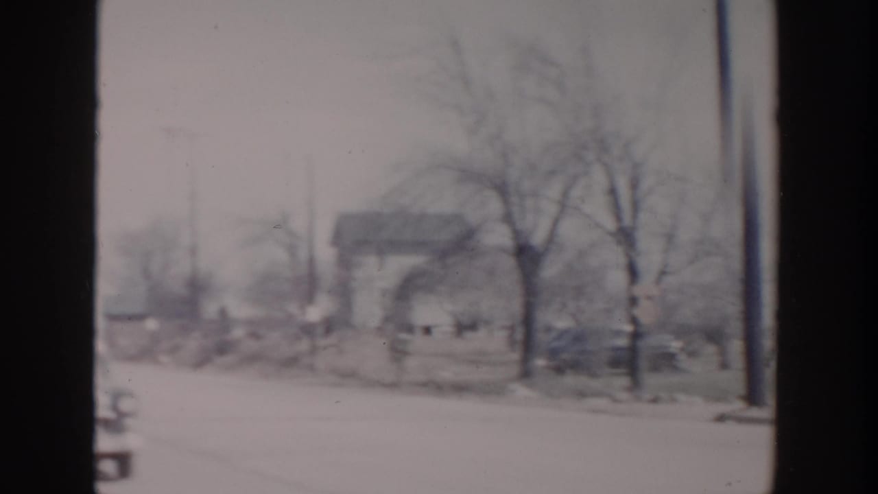 1956 Grand Rapids home-movie frame showing a snow-covered roadside, bare trees, and a distant house in soft focus.