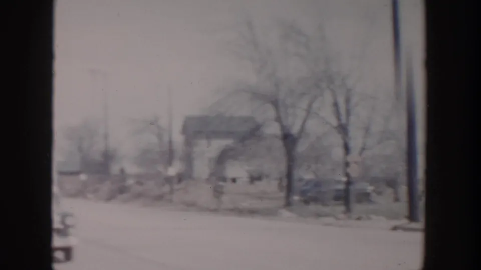 1956 Grand Rapids home-movie frame showing a snow-covered roadside, bare trees, and a distant house in soft focus.