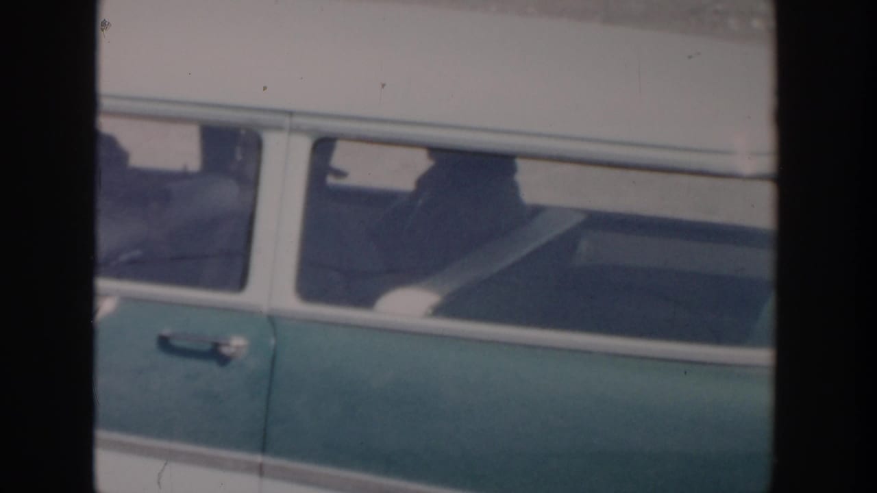 Green and white station wagon passing close to the camera.