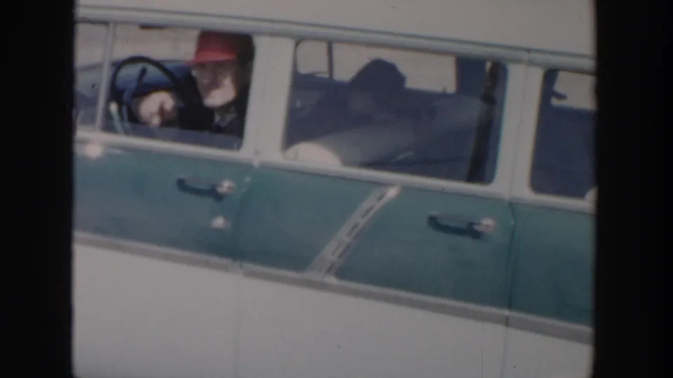 A man in a red cap is seen at the open window of a green and white station wagon in Michigan home-movie footage.