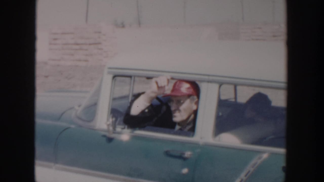 In 1956 Grand Rapids home-movie footage, a man in a red cap waves from inside a teal-and-white 1950s sedan.