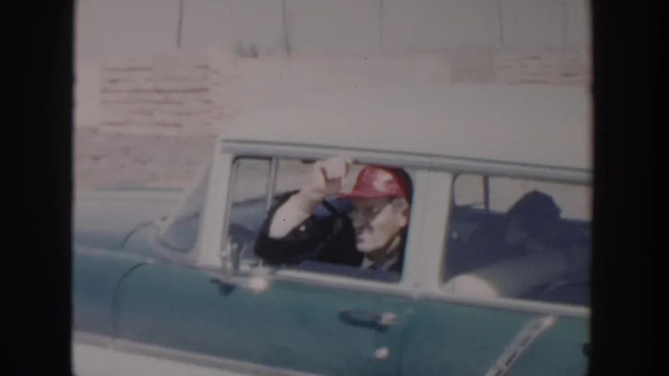In 1956 Grand Rapids home-movie footage, a man in a red cap waves from inside a teal-and-white 1950s sedan.