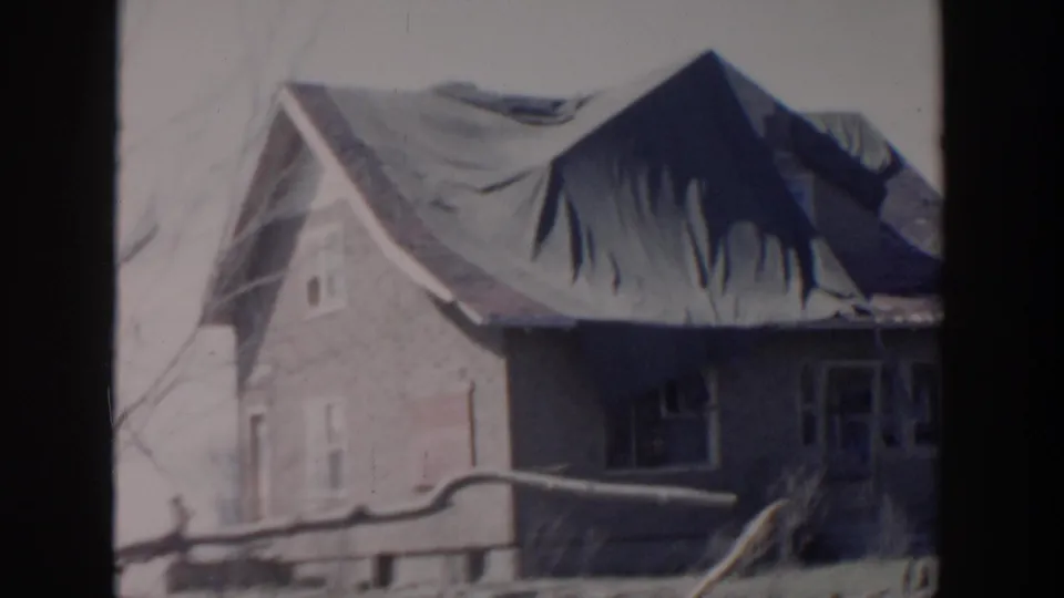 A brick house in the supplied Grand Rapids footage appears with a dark tarp covering much of the roof and bare branches nearby.