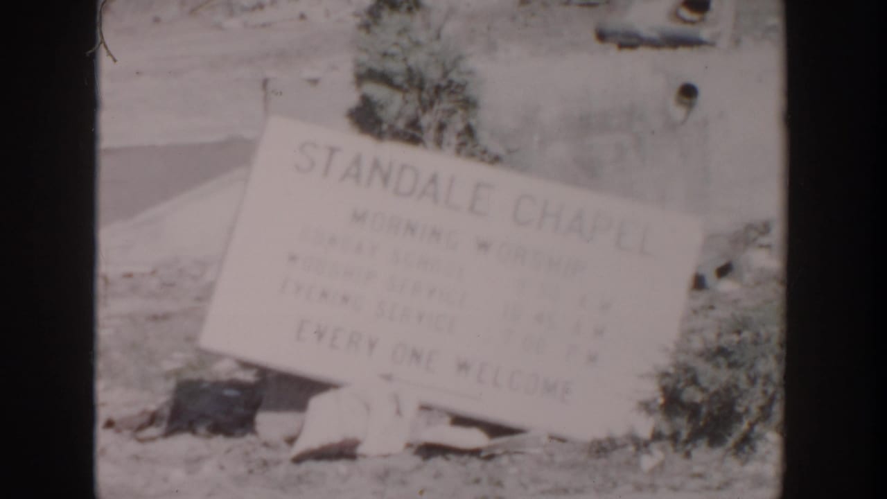 1956 Grand Rapids 8mm frame showing a fallen Standale Chapel sign near a damaged exterior wall and scattered rubble.
