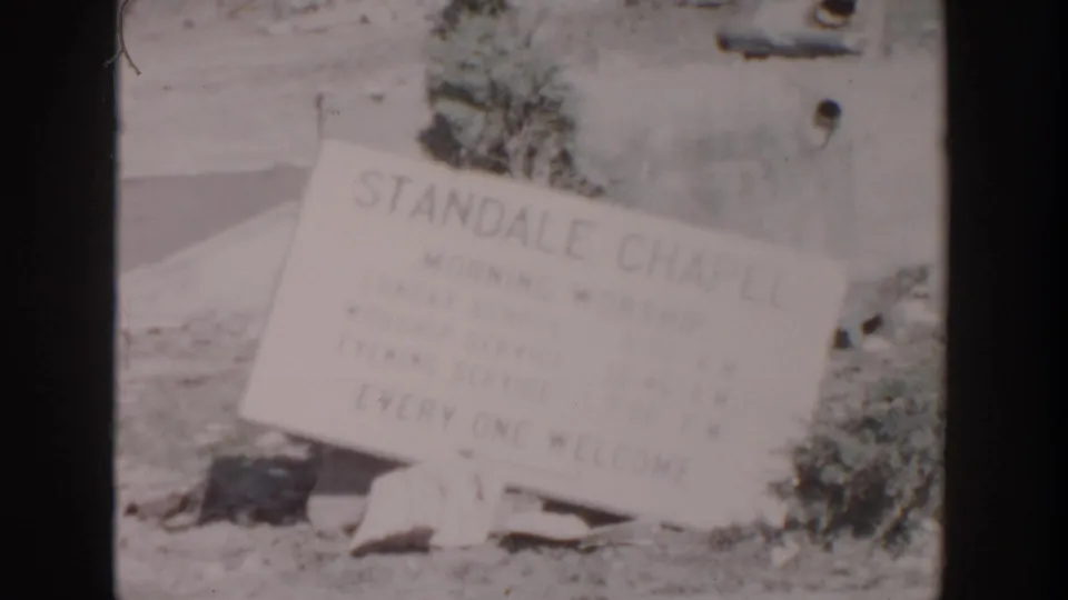 1956 Grand Rapids 8mm frame showing a fallen Standale Chapel sign near a damaged exterior wall and scattered rubble.